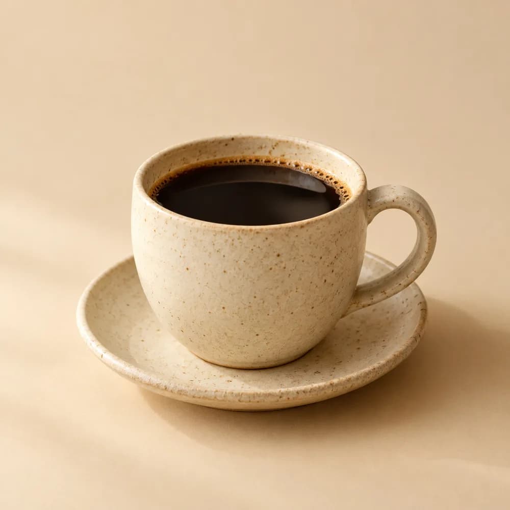 A speckled ceramic cup of black pour-over coffee on a saucer